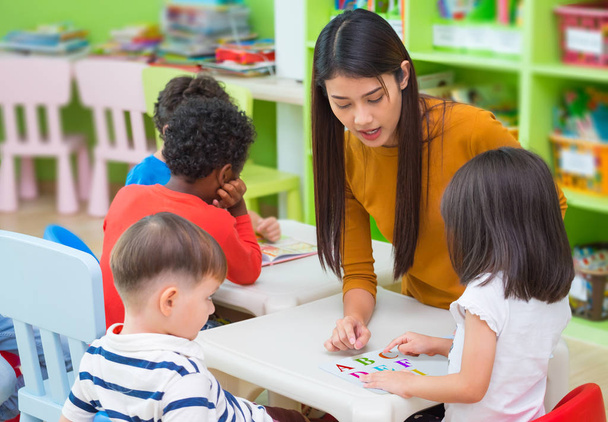 Asian female teacher teaching mixed race kids reading book in cl - Fotografie, Obrázek