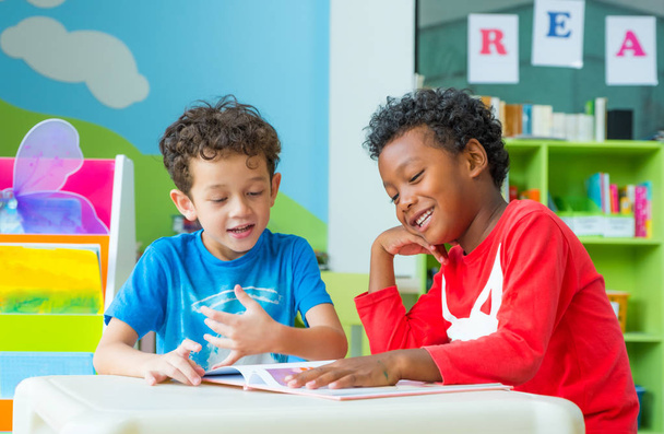 Two boy kid sit on table and reading tale book  in preschool lib - Photo, image