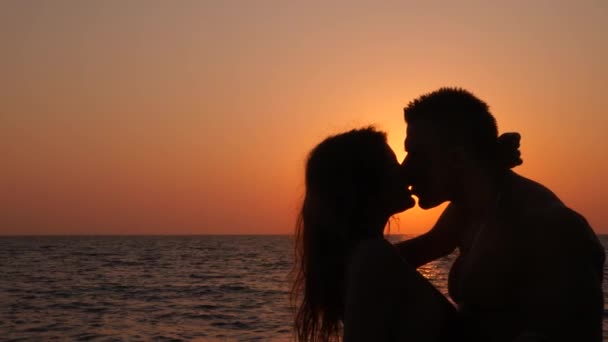 Silhouettes of pregnant women in bikini and romantic muscular man. the bodybuilder hugs, kisses his wife and strokes her belly. against the background of a sea sunset. 4k. Slow motion - Footage, Video