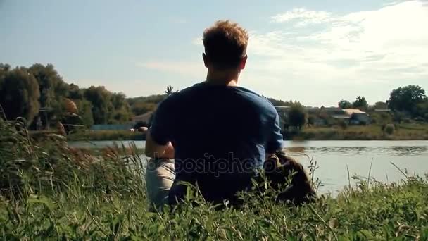 göl ve video görüntüleri yeni benzersiz kalite insanların seyahat güzel manzara gözlemleyerek yukarıda yeşil çimenlerin üzerinde uzun boylu Beyaz sarışın güçlü erkek adam oturur - Video, Çekim