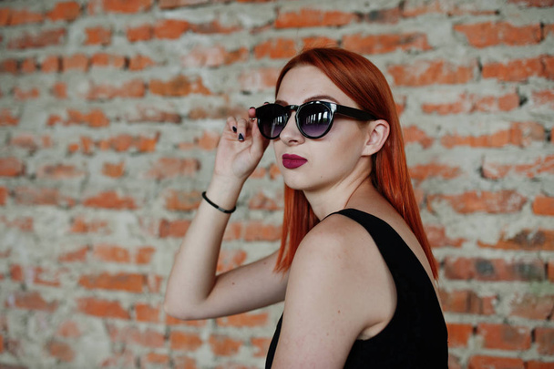 Red haired stylish girl in sunglasses wear in black, against aba - Fotoğraf, Görsel