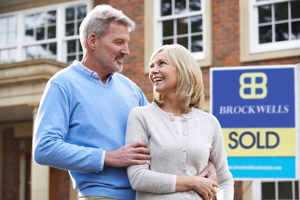 Happy Mature Couple Standing Outside House With Sold Sign - Photo, image