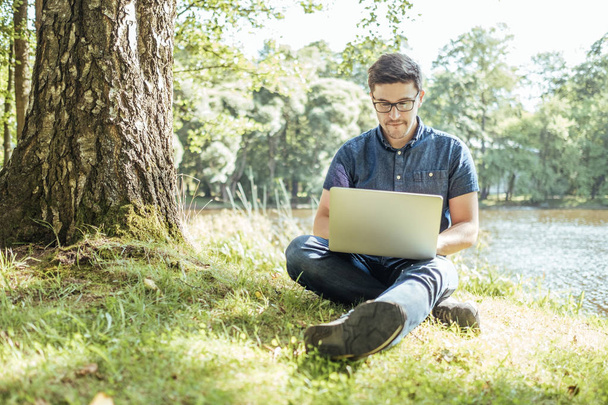 Young man with laptop outdoor sitting on the grass - 写真・画像