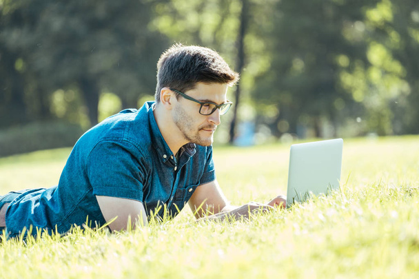 Young man lying on grass and using laptop - Foto, imagen
