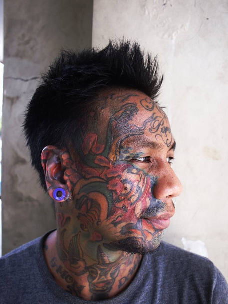 Um homem com arte corporal mostra sua tatuagem facial e piercing na orelha
. - Foto, Imagem