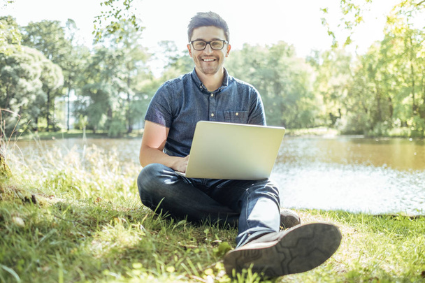 Jovem com laptop ao ar livre sentado na grama
 - Foto, Imagem