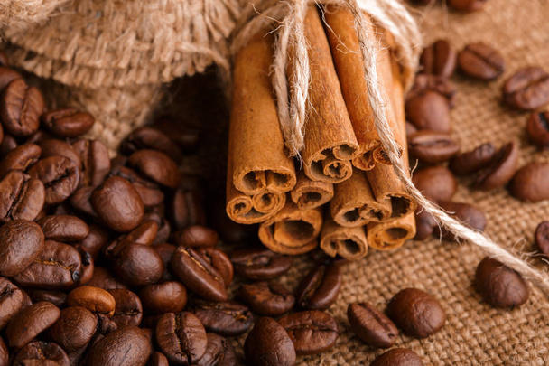 Coffee beans and cinnamon on a background of burlap. Roasted coffee beans background close up. Coffee beans pile from top with copy space for text. Seasoning. Spice. Cinnamon. Badian. Coffee house. - Fotografie, Obrázek