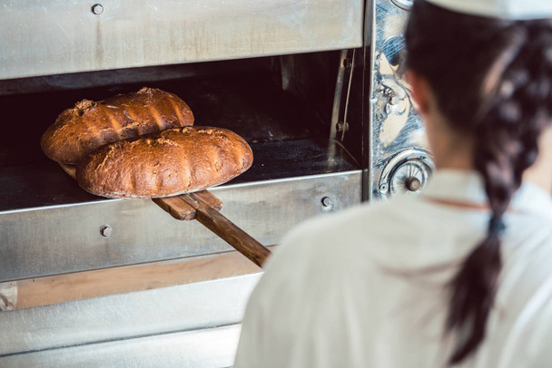 Panadero conseguir pan fresco con pala fuera del horno
 - Foto, imagen