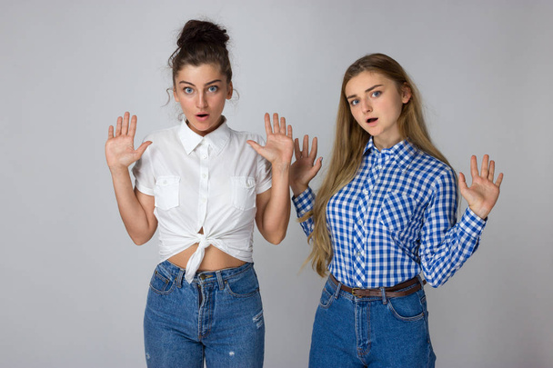 zwei junge Schwestern stehen mit erhobenen Händen zur Seite und zucken mit den Schultern, ohne den Mut zu haben, eine Entscheidung über den grauen Hintergrund zu treffen - Foto, Bild