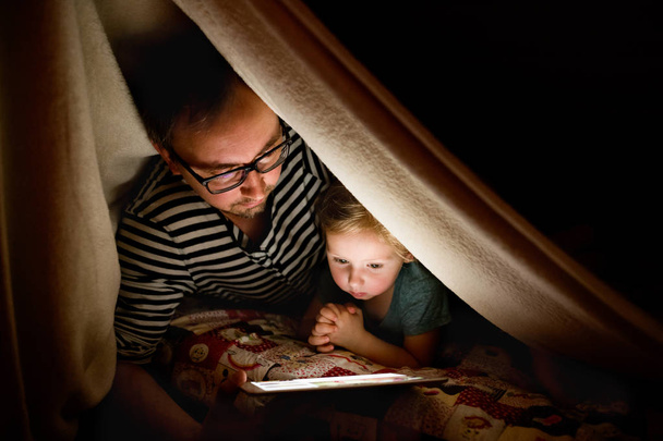 Father with tablet and little daughter at home at night. - Фото, изображение
