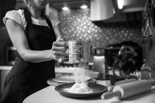 Woman sifting flour through sieve. Selective focus - Zdjęcie, obraz