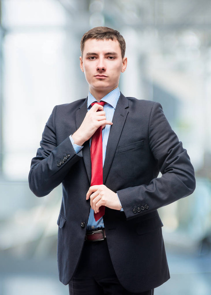 Homme en costume corrige cravate rouge, portrait au bureau
 - Photo, image