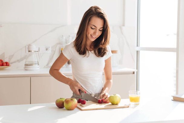 Happy healthy woman cutting fruits on a wooden board - Foto, Bild