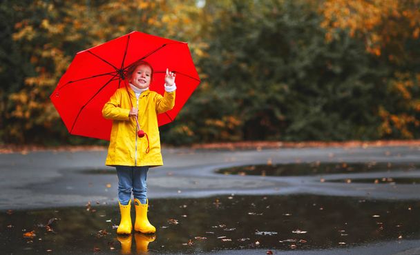 happy child girl with an umbrella and rubber boots in puddle  on - Photo, Image