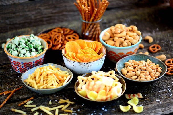 Verschillende soorten snacks - chips, gezouten pinda's, cashewnoten, erwten met wasabi, pretzels met zout, aardappelen, gezouten stro. - Foto, afbeelding