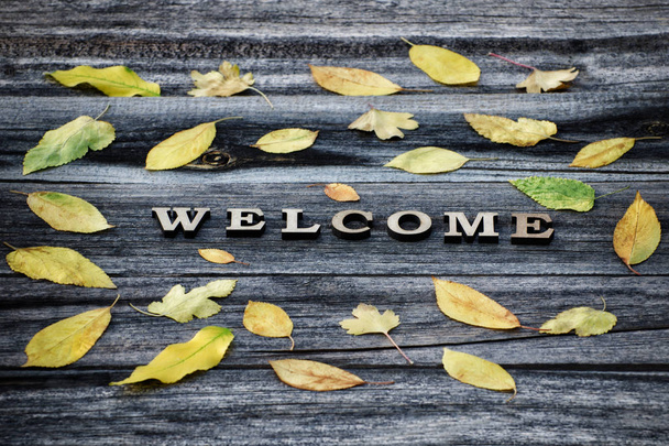 Word Welcome, wooden letters. Frame of yellow leaves, wooden background - Fotoğraf, Görsel