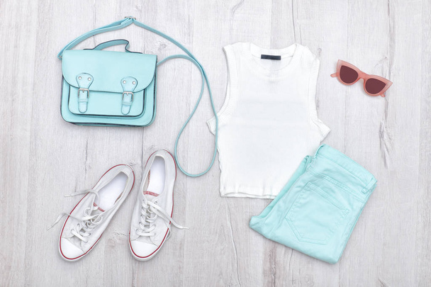 Λευκή κορυφή, μέντα-χρωματισμένα jeans, λευκά αθλητικά παπούτσια και τσάντα. Έννοια της μόδας. Ξύλινο υπόβαθρο. - Φωτογραφία, εικόνα