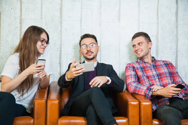 Group of three young people hold smartphones talk and smile - Φωτογραφία, εικόνα