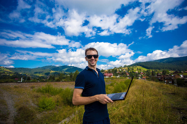Ένας νεαρός άνδρας που εργάζεται σε ένα φορητό υπολογιστή, που είναι υψηλή στα βουνά - Φωτογραφία, εικόνα