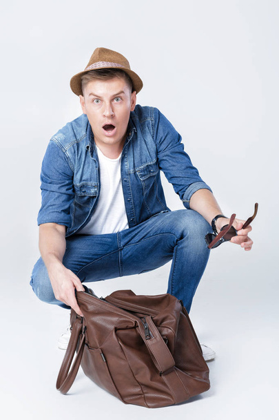surprised man in a hat looks in an empty leather bag. - Foto, Imagem