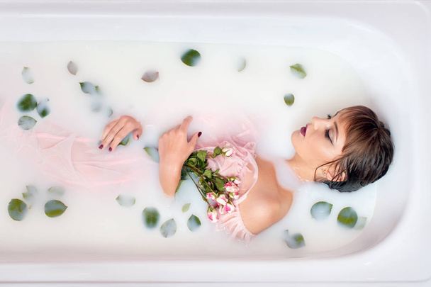 Молода дівчина приймає ванну з молоком і пелюстками троянд
. - Фото, зображення