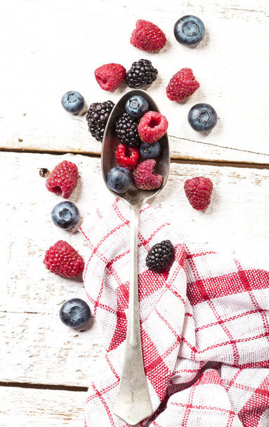 Ripe and sweet berries on vintage metal spoon on wooden white background - Photo, Image