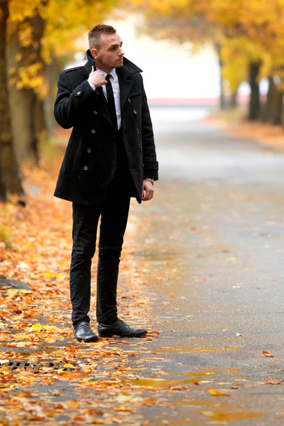 Aantrekkelijke man in zwarte jas in herfst bos. - Foto, afbeelding
