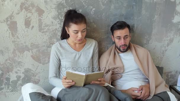 Young lady reading her ill husband book - Filmati, video