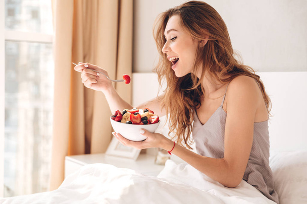 Young lady in pajamas eating breakfast in bed - Foto, imagen