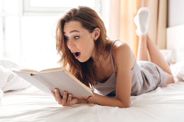 Shocked pretty lady lies on bed indoors - Foto, Imagem