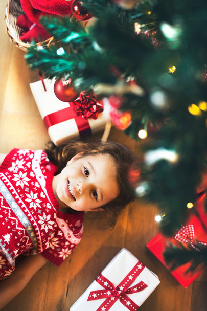 Little girl lying under Christmas tree among presents, - Фото, зображення