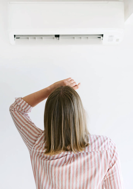 Women dying from the heat standing in front of the air conditioner. - Photo, Image