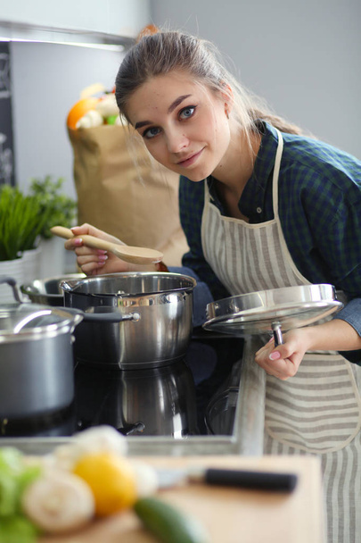 Young woman standing by the stove in the kitchen . - Фото, изображение