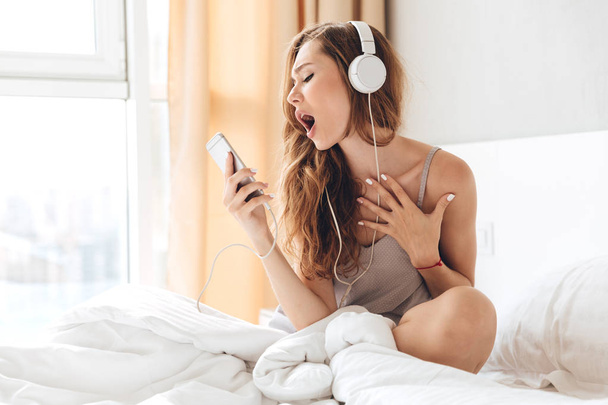 Young woman listening music and singing in bed - Foto, immagini