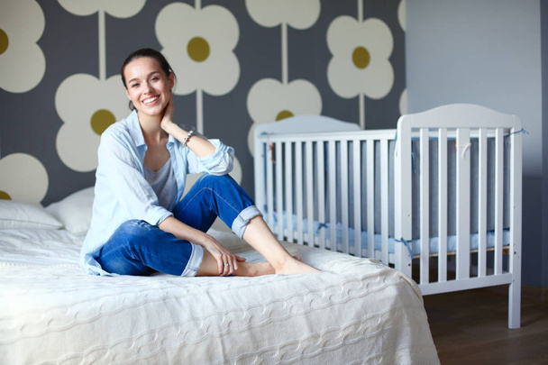 Young woman sitting on the bed near childrens cot. Young mom - Фото, зображення