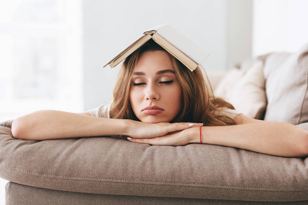 ソファの上の頭の上の本の若い女性睡眠 - 写真・画像