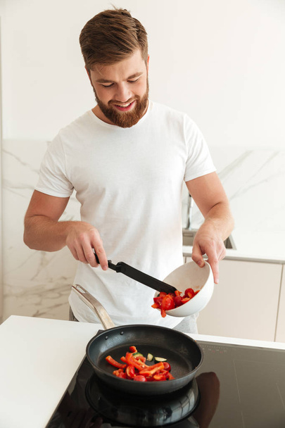 Vertical image of happy bearded man cooking vegetables - Foto, immagini