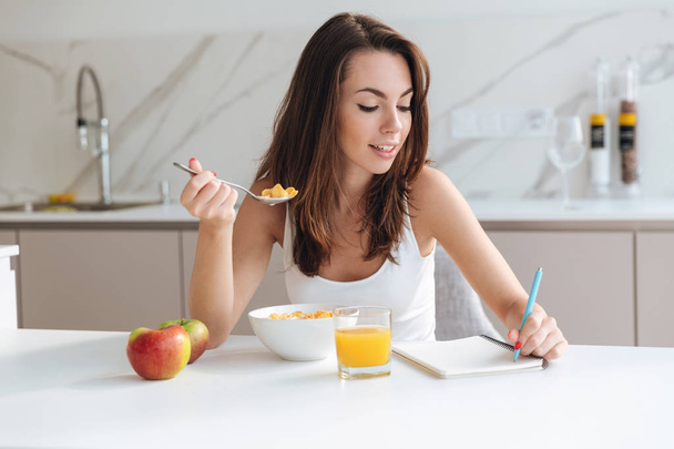 Smiling attractive woman eating corn flakes cereal for breakfast - Fotó, kép