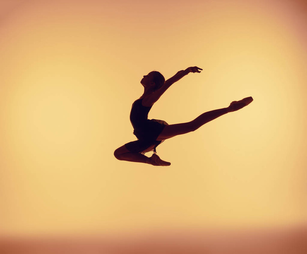 Beautiful young ballet dancer jumping on a orange background. - Фото, зображення