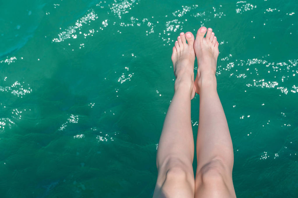young female legs hanging over the sea water - Photo, image
