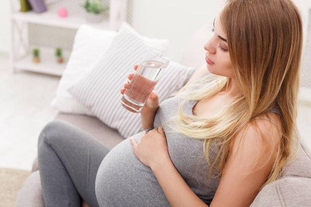 Schwangere mit Glas Wasser auf Sofa in Nahaufnahme - Foto, Bild