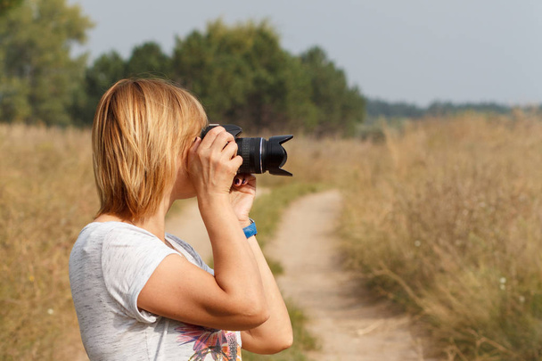 Young woman holding digital camera and taking pictures - Foto, afbeelding