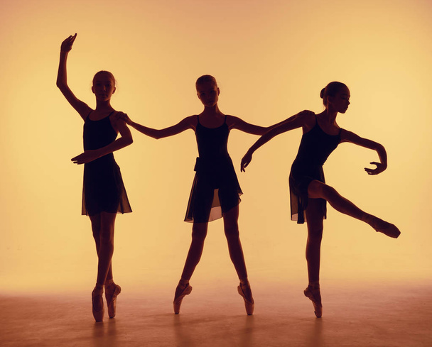 Composition from silhouettes of three young dancers in ballet poses on a orange background. - Fotografie, Obrázek