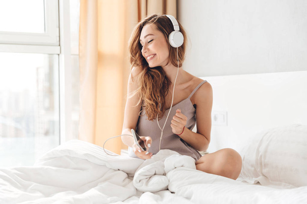 Carefree lady in pajamas listening music with headphones - Foto, imagen