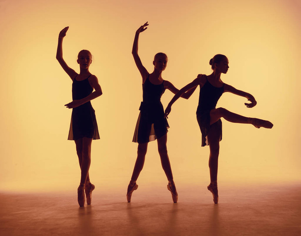 Composition from silhouettes of three young dancers in ballet poses on a orange background. - Photo, Image