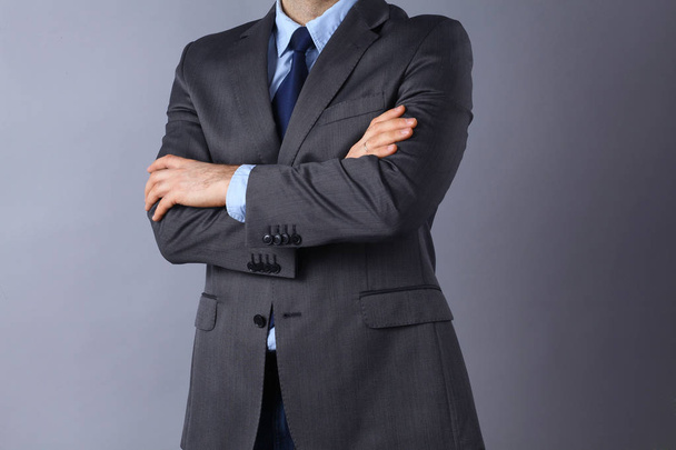 Young businessman standing with arms crossed on gray background - Photo, image