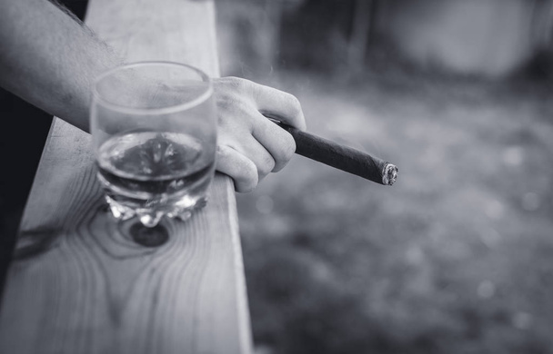 man holding a cigar and standing next to whiskey - Фото, изображение