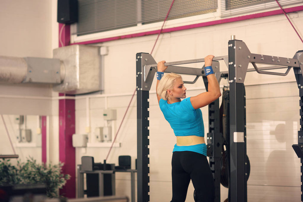 Bodybuilding. Strong fit woman exercising in a gym - doing pull-ups with weight - Photo, Image