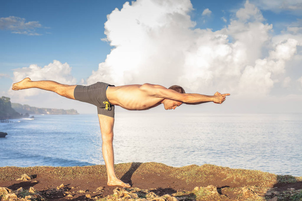 Handsome man doing yoga at cliff with blue sea background - Fotoğraf, Görsel