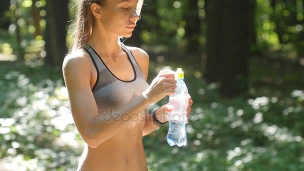 Фитнес-женщина пьет воду из бутылки в солнечном лесу
 - Кадры, видео